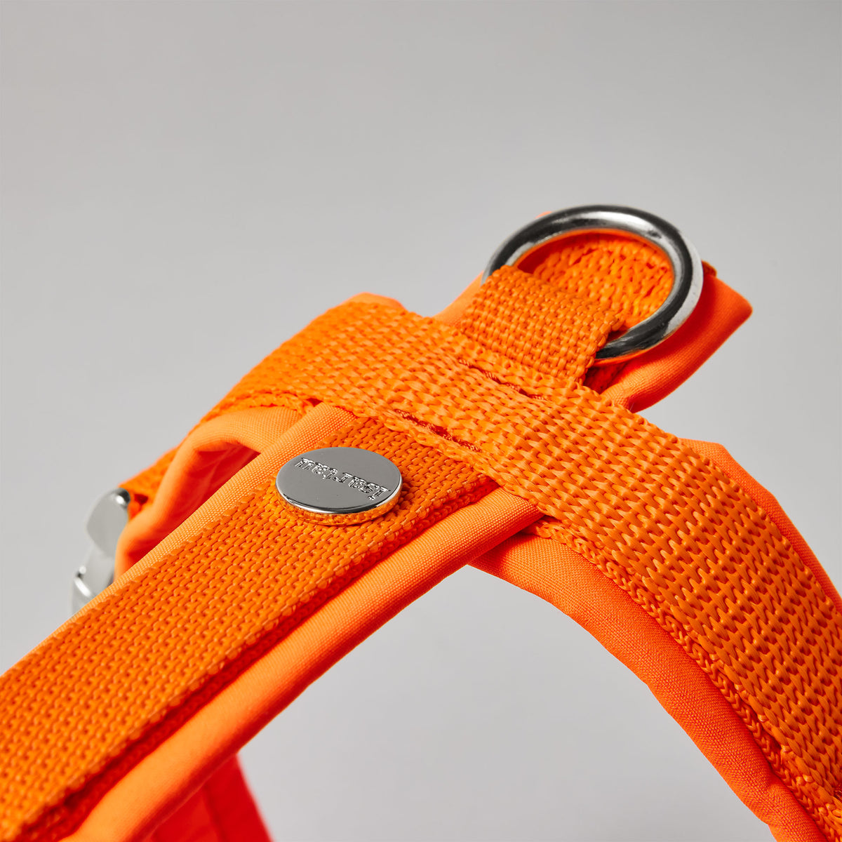Rückenstück des neonorangen Hundegeschirrs mit gepolstertem O-Ring zum Einhaken des Karabiners und Logo-Niete