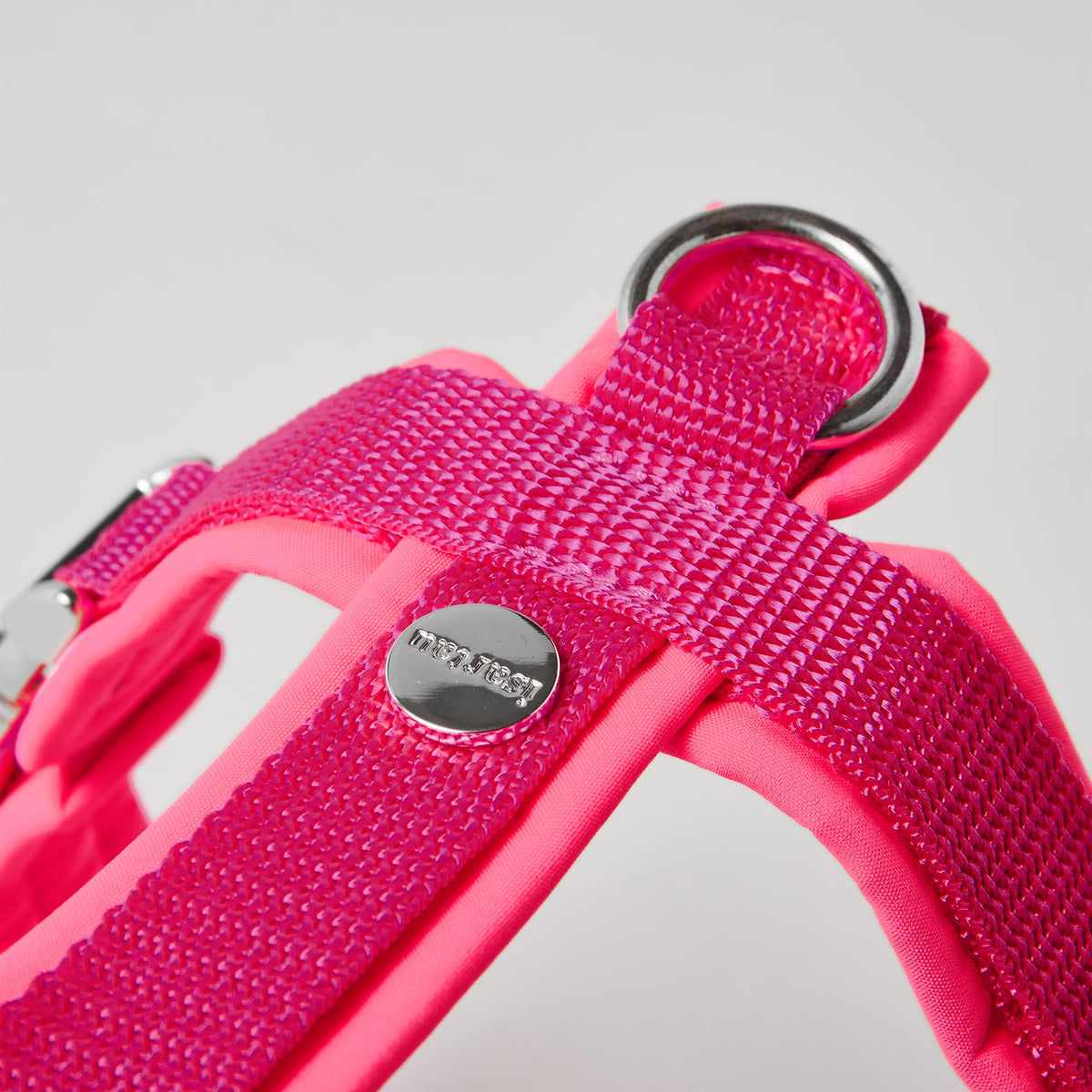Rückenstück des neonpinken Hundegeschirrs mit gepolstertem O-Ring zum Einhaken des Karabiners und Logo-Niete
